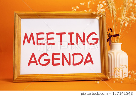 Meeting agenda symbol. Concept words Meeting agenda on beautiful wooden picture frame. Beautiful orange background with flower vase. Business and Meeting agenda concept. Copy space. 137141548