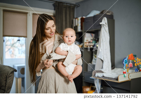 Mother holds baby in living room and smiles during quiet afternoon at home in early spring 137141792