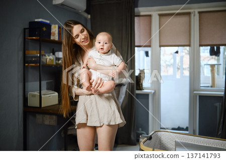 Mother holds baby in apartment with sunlight shining through windows Mother holds baby in apartment with sunlight shining through windows 137141793