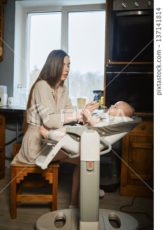 Mother spoon feeds her baby with baby food 137141814