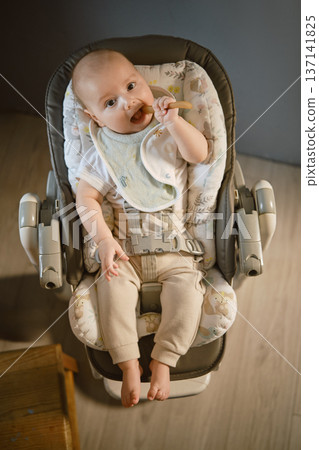 Baby sitting in a high chair enjoying a snack in a quiet room 137141825