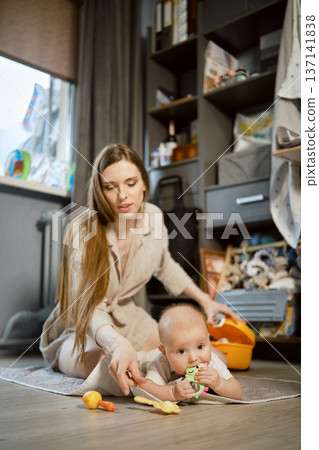 Mother and baby play on the floor in a living room during daytime Mother and baby play on the floor in a living room during daytime 137141838