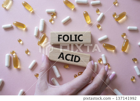 Folic acid symbol. Wooden blocks with words Folic acid. Beautiful pink background with pills. Doctor hand. Medicine and Folic acid concept. Copy space. 137141992