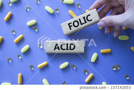 Folic acid symbol. Wooden blocks with words Folic acid. Beautiful purple background with pills. Doctor hand. Medicine and Folic acid concept. Copy space. Folic acid symbol. Wooden blocks with words Folic acid. Beautiful purple background with pills. Doctor hand. Medicine and Folic acid concept. Copy space. 137142053
