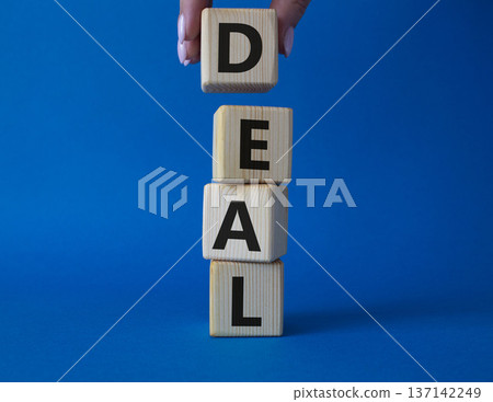 Deal symbol. Concept word Deal on wooden cubes. Businessman hand. Beautiful blue background. Business and Deal concept. Copy space. Deal symbol. Concept word Deal on wooden cubes. Businessman hand. Beautiful blue background. Business and Deal concept. Copy space. 137142249