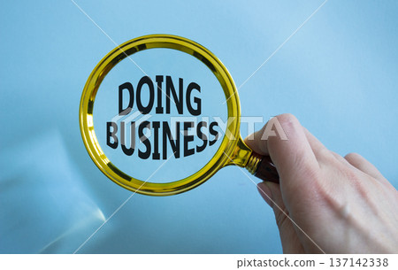 Doing Business symbol. Magnifying Glass with Concept word Doing Business. Businessman hand. Beautiful blue background. Business and Doing Business concept. Copy space Doing Business symbol. Magnifying Glass with Concept word Doing Business. Businessman hand. Beautiful blue background. Business and Doing Business concept. Copy space 137142338