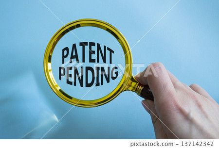 Patent Pending symbol. Magnifying Glass with Concept word Patent Pending. Businessman hand. Beautiful blue background. Business and Patent Pending concept. Copy space 137142342