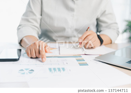 Business professional using calculator and pen reviewing financial report charts on office desk, budgeting and accounting analysis for planning, audit and fintech management workflow. financial report Business professional using calculator and pen reviewing financial report charts on office desk, budgeting and accounting analysis for planning, audit and fintech management workflow. financial report 137144711