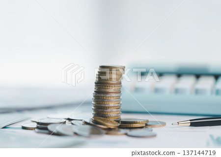Stacks of coins on financial report with charts, blurred calculator in background, symbolizing savings, investment growth, budgeting and wealth management for business planning strategy. saving Stacks of coins on financial report with charts, blurred calculator in background, symbolizing savings, investment growth, budgeting and wealth management for business planning strategy. saving 137144719