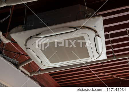 Store interior with ceiling-mounted air conditioner and exposed piping. Modern interior with built-in air conditioning equipment and skeleton ceiling. Store interior with ceiling-mounted air conditioner and exposed piping. Modern interior with built-in air conditioning equipment and skeleton ceiling. 137145984