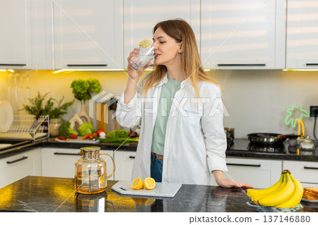 Middle-aged woman drinking lemon water in home kitchen for hydration wellness diet weight loss plan Middle-aged woman drinking lemon water in home kitchen for hydration wellness diet weight loss plan 137146880