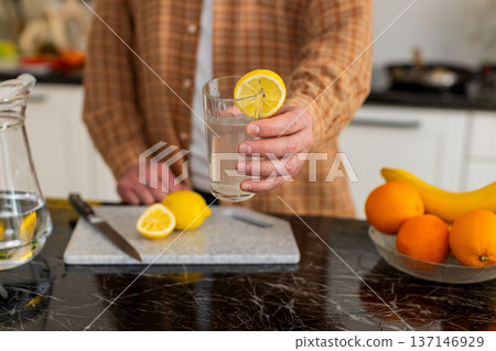Unrecognizable man making lemon water in kitchen for healthy hydration morning wellness routine Unrecognizable man making lemon water in kitchen for healthy hydration morning wellness routine 137146929