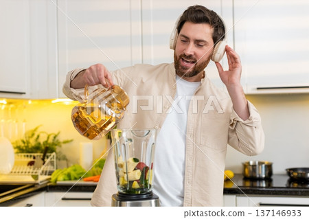 Middle-aged man pouring water into blender for green smoothie listening to music in home kitchen joy 137146933