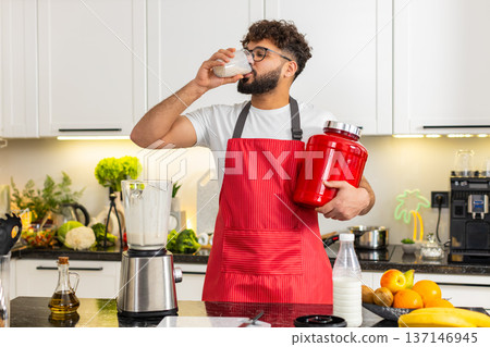 Arabian young adult man pours whey protein smoothie into glass and drinks after workout in kitchen 137146945