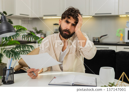 Indian man reading official letter facepalm stressed about finances writing action plan in notebook Indian man reading official letter facepalm stressed about finances writing action plan in notebook 137147001