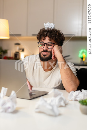 Arabian man fights creative block writes ideas for project crumpled papers desk frustrated evening Arabian man fights creative block writes ideas for project crumpled papers desk frustrated evening 137147009