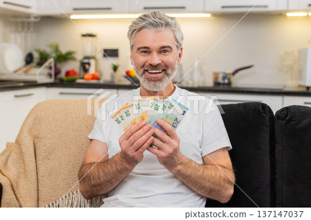 Middle-aged man counts money cash euros smiles at big plans purchase salary bonus savings investment 137147037