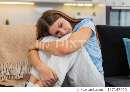 Young woman sits hugging knees sad after bad news stressed upset low mood anxious and lonely relief Young woman sits hugging knees sad after bad news stressed upset low mood anxious and lonely relief 137147053