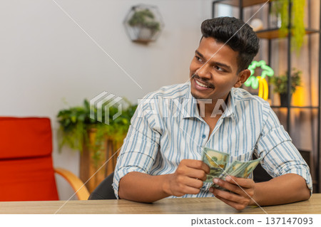 Indian man counts dollars smiles at bonus salary plans invest save proud of earnings profit wealth Indian man counts dollars smiles at bonus salary plans invest save proud of earnings profit wealth 137147093