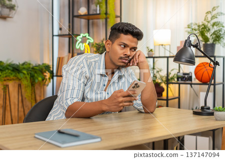 Indian man scrolls smartphone news feed bored frown unhappy tired mood burnout from endless updates Indian man scrolls smartphone news feed bored frown unhappy tired mood burnout from endless updates 137147094
