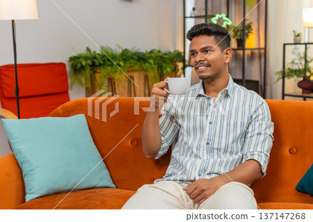 Indian man enjoys hot tea or coffee cup relax morning feeling energy boost calm mood happy start day Indian man enjoys hot tea or coffee cup relax morning feeling energy boost calm mood happy start day 137147268