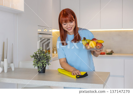 Young woman wipes kitchen countertop with microfiber cloth polishes surface shows clean tidy order Young woman wipes kitchen countertop with microfiber cloth polishes surface shows clean tidy order 137147270