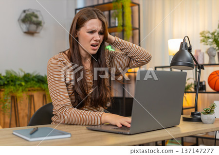 Young woman works on laptop sees game loss failed bet and grim news sighs feels upset disappointed 137147277