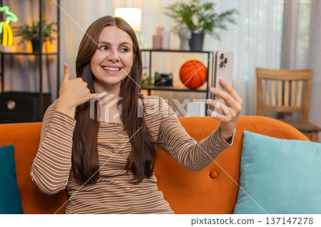 Young woman on smartphone video call shows call me sign blows kiss then laughs and looks at camera Young woman on smartphone video call shows call me sign blows kiss then laughs and looks at camera 137147278