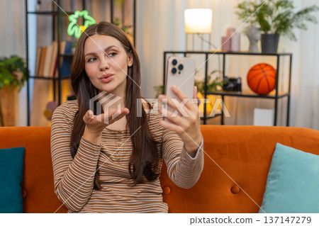 Young woman on smartphone video call shows call me sign blows kiss then laughs and looks at camera 137147279