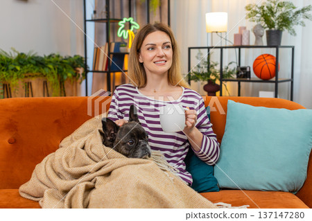 Middle-aged woman with dog drinks tea and covers with plaid blanket warm calm rest and cozy vibe 137147280