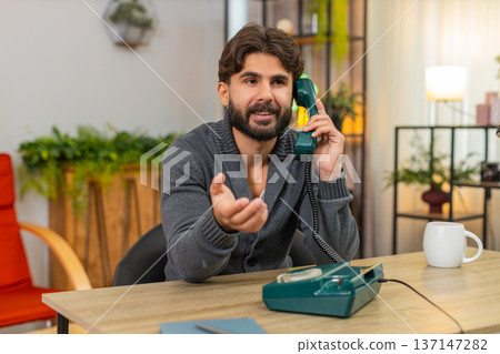 Indian man talks on retro wired telephone from nineties smiles places handset back on base with care Indian man talks on retro wired telephone from nineties smiles places handset back on base with care 137147282