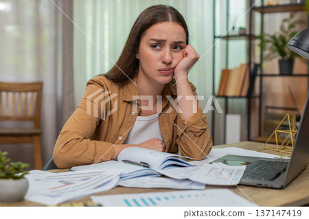 Young woman holding head over unpaid bills scattered near laptop and calculator showing deep despair Young woman holding head over unpaid bills scattered near laptop and calculator showing deep despair 137147419