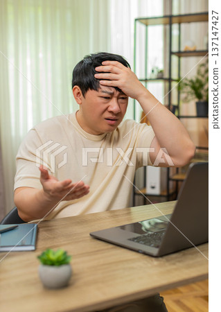 Asian man facepalming after absurd news on laptop, showing disbelief, frustration, annoyed reaction Asian man facepalming after absurd news on laptop, showing disbelief, frustration, annoyed reaction 137147427