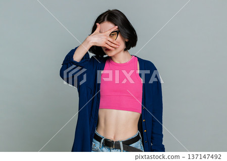 Woman playfully spying through hand shaped like binoculars smiling humorously indicating curiosity 137147492