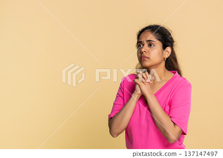 Indian woman with hands clasped in prayer, looking upward with hopeful expression and sincerity 137147497