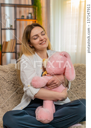 Woman hugging plush toy at home smiling with comfort and calmness feeling safe emotionally grounded 137147911