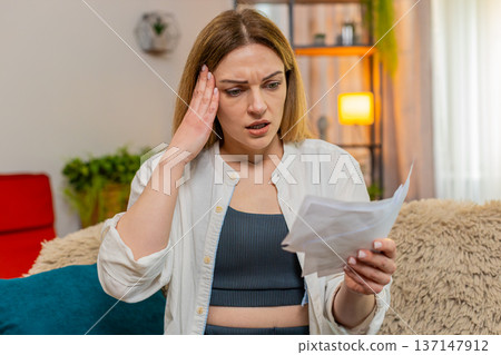 Adult woman reacting to financial stress at home reading utility bills sad worried expression stress Adult woman reacting to financial stress at home reading utility bills sad worried expression stress 137147912