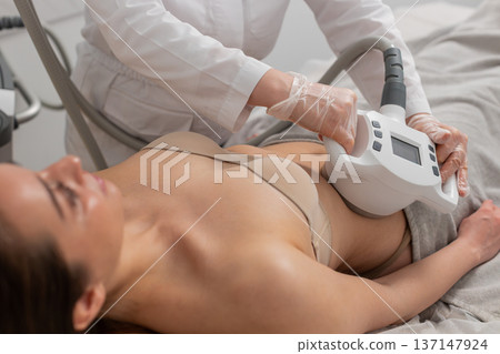Caucasian woman receives abdomen vacuum massage from cosmetologist using LPG device in beauty clinic Caucasian woman receives abdomen vacuum massage from cosmetologist using LPG device in beauty clinic 137147924