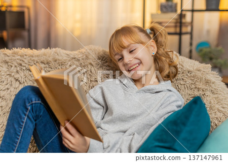 Young small teenager girl reading favorite storybook at home sofa quiet smiles, tiny serious sighs 137147961
