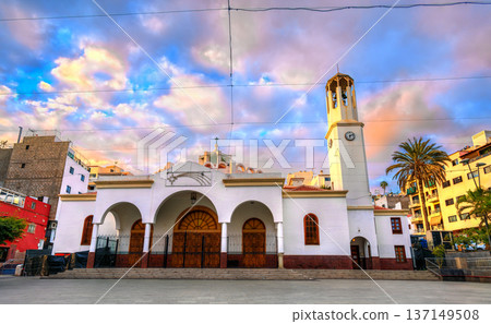 Scenic view of the white facade and bell tower of the Parroquia Nuestra Senora del Carmen church under a colorful sky in Los Cristianos, Tenerife. Scenic view of the white facade and bell tower of the Parroquia Nuestra Senora del Carmen church under a colorful sky in Los Cristianos, Tenerife. 137149508