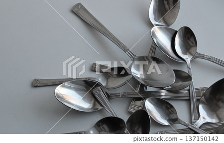 Big And Small Metallic Spoons Scattered On White At A Side Of Image With Clean Part For Title Or Logo. Dishware Concept Design Stock Photo Big And Small Metallic Spoons Scattered On White At A Side Of Image With Clean Part For Title Or Logo. Dishware Concept Design Stock Photo 137150142