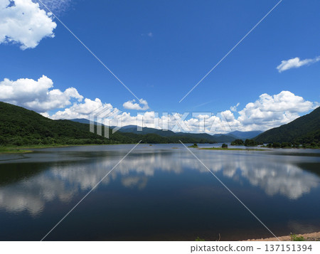 Early summer at Lake Akimoto in Urabandai. The white cumulonimbus clouds reflected on the vast blue lake surface against the green islets and mountain ranges are striking and beautiful. Early summer at Lake Akimoto in Urabandai. The white cumulonimbus clouds reflected on the vast blue lake surface against the green islets and mountain ranges are striking and beautiful. 137151394