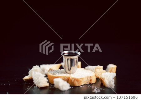 Communion still life with bread on a wooden plate, red wine in a small cup and ornate chalice beside a Holy Bible on dark table, symbolizing Eucharist, worship, faith and remembrance with copy space. Communion still life with bread on a wooden plate, red wine in a small cup and ornate chalice beside a Holy Bible on dark table, symbolizing Eucharist, worship, faith and remembrance with copy space. 137151696