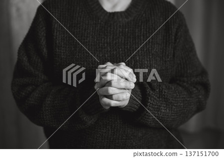 Black and white close-up of clasped hands resting on a table, suggesting prayer, contemplation and quiet faith. Minimal background with copy space for message. Spiritual mood for inspirational text. 137151700