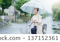 Smiling young Japanese woman riding a bicycle with an umbrella on a rainy day 137152361