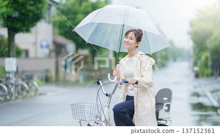 下雨天，一位面帶微笑的日本年輕女子騎著腳踏車，撐著傘。 137152361