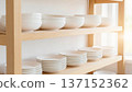 White tableware and ceramic bowls lined up on a clean wooden shelf 137152362