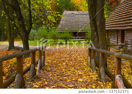Charming wooden bridge leads to rustic village houses in vibrant autumn forest Charming wooden bridge leads to rustic village houses in vibrant autumn forest 137152371