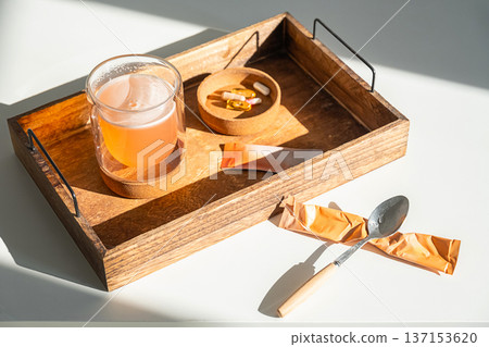 Glass of healthy drink on wooden tray with white vitamins in bowl and orange powder sachets. 137153620