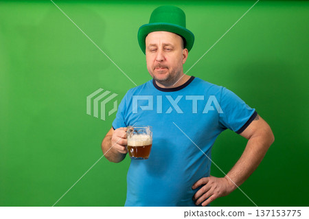 Man wearing green leprechaun hat holding beer mug against green backdrop. St. Patricks Day festive attire with Irish pub theme. Holiday celebration and casual drinking concept. photography Man wearing green leprechaun hat holding beer mug against green backdrop. St. Patricks Day festive attire with Irish pub theme. Holiday celebration and casual drinking concept. photography 137153775